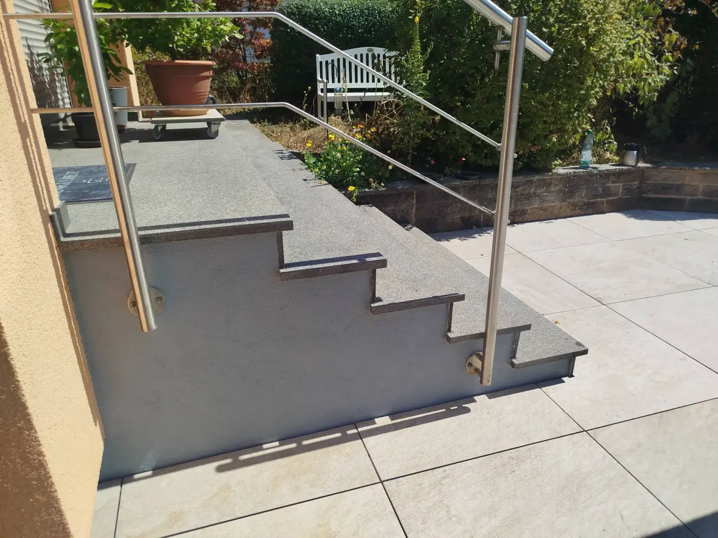 Aussentreppe mit Granitstufen und Edelstahlgeländer neben einer Terrasse aus hellen Platten