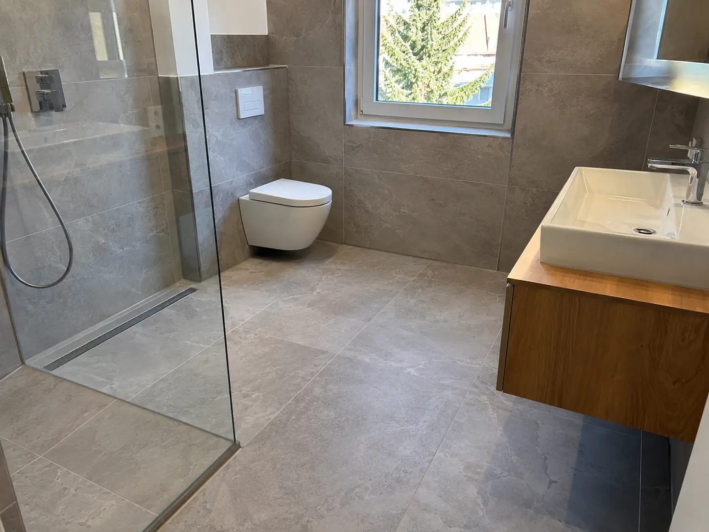 Bad mit bodengleicher Dusche, Glaswand, wandhängendem WC und großformatigen Fliesen in Steinoptik