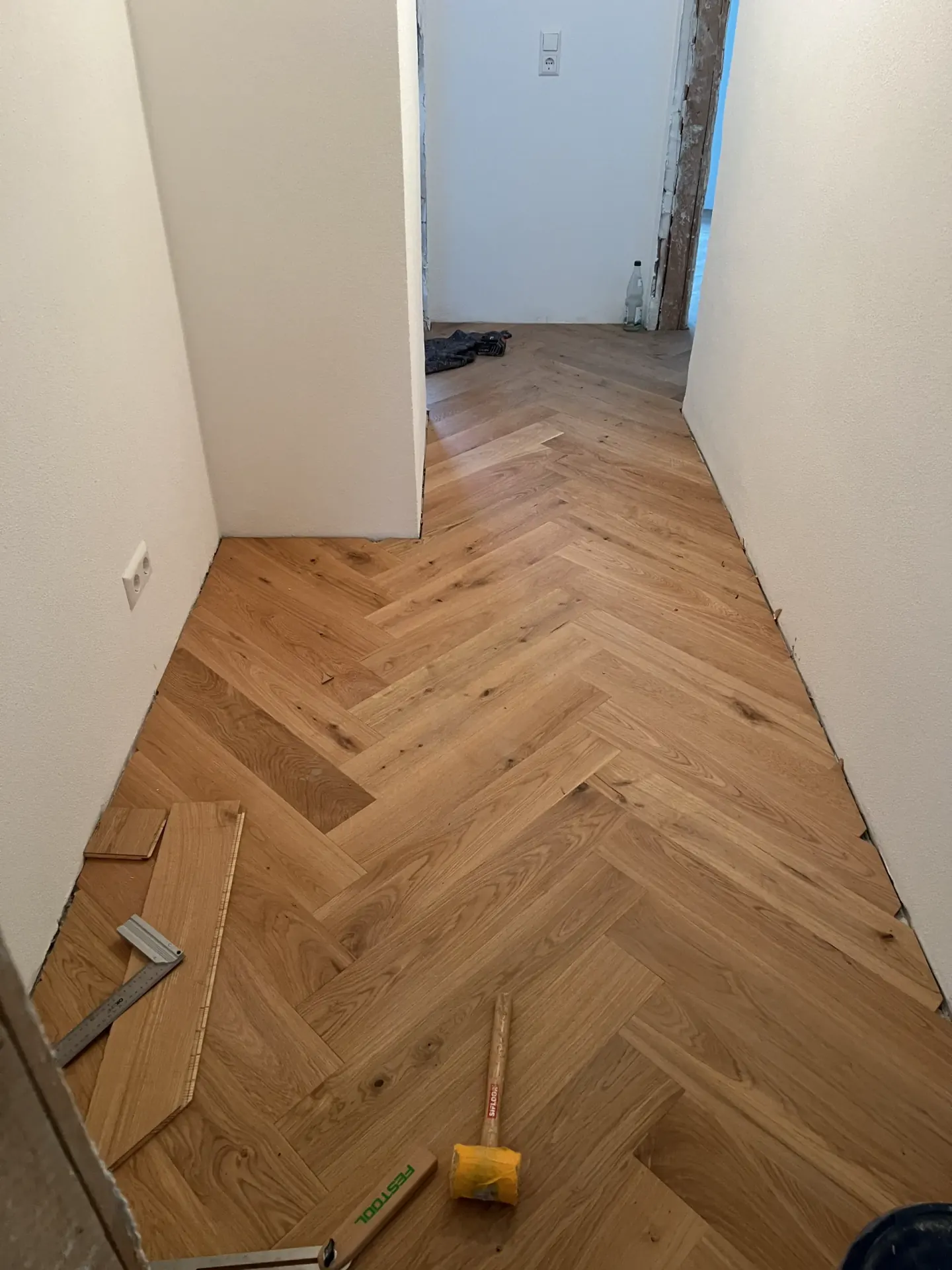 Holzboden im Fischgrätmuster wird im Flur verlegt, davor liegen Winkel und Hammer