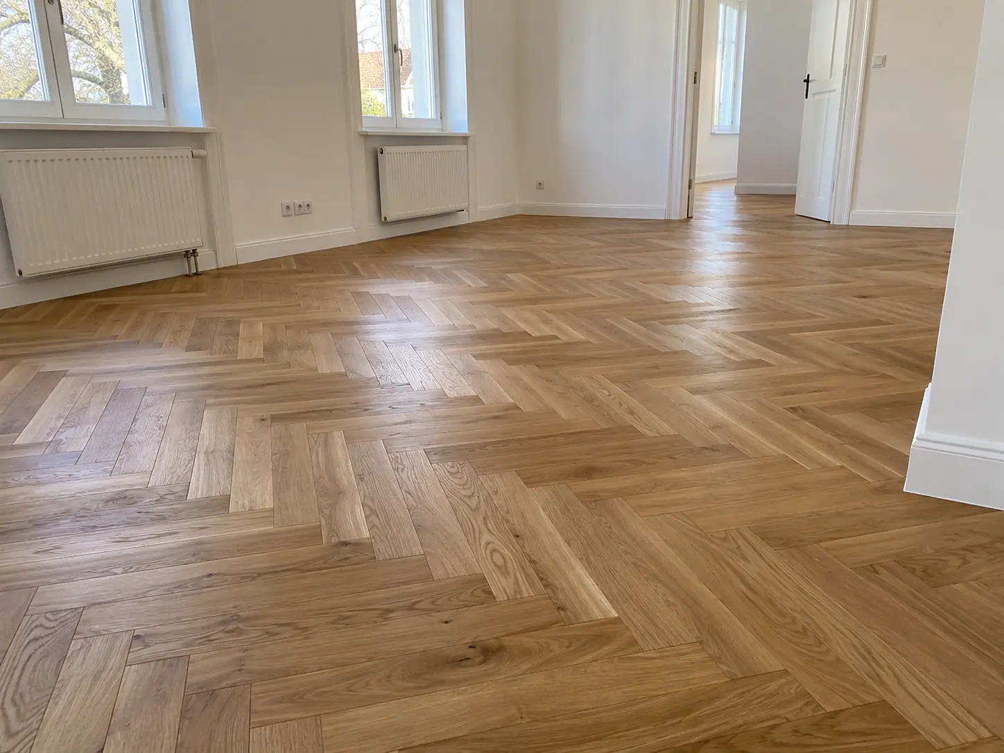 Holzboden im Fischgrätmuster in einem hellen Wohnraum mit hohen Fenstern