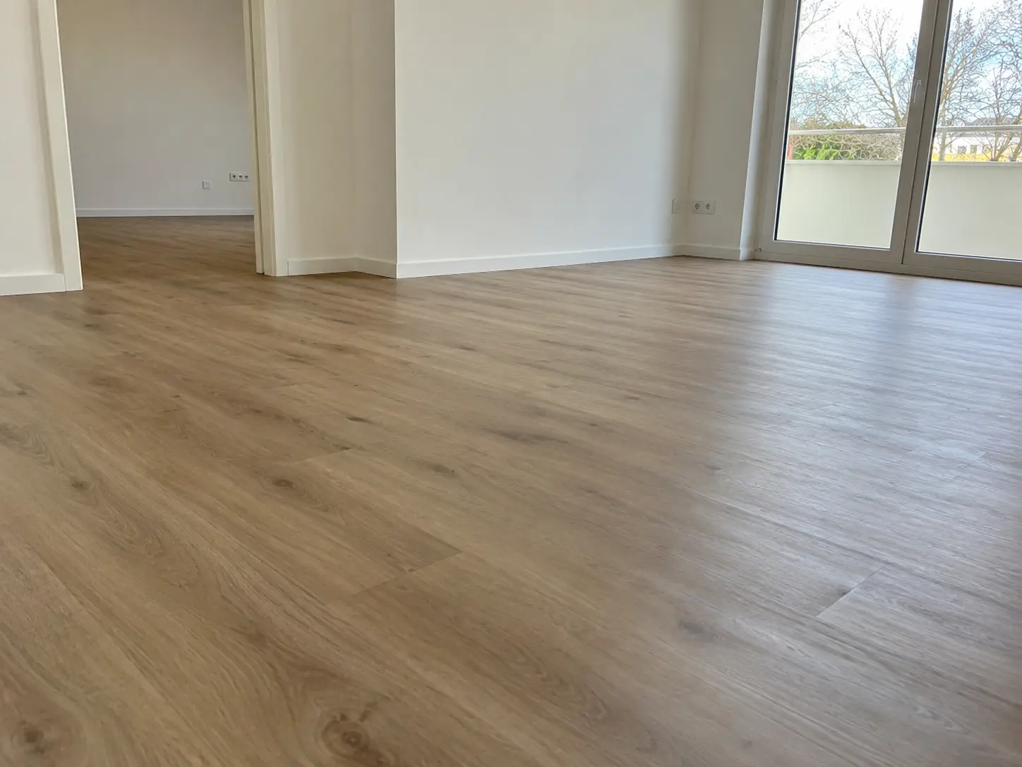 Heller Wohnraum mit neu verlegtem Laminat in Holzoptik und bodentiefen Fenstern