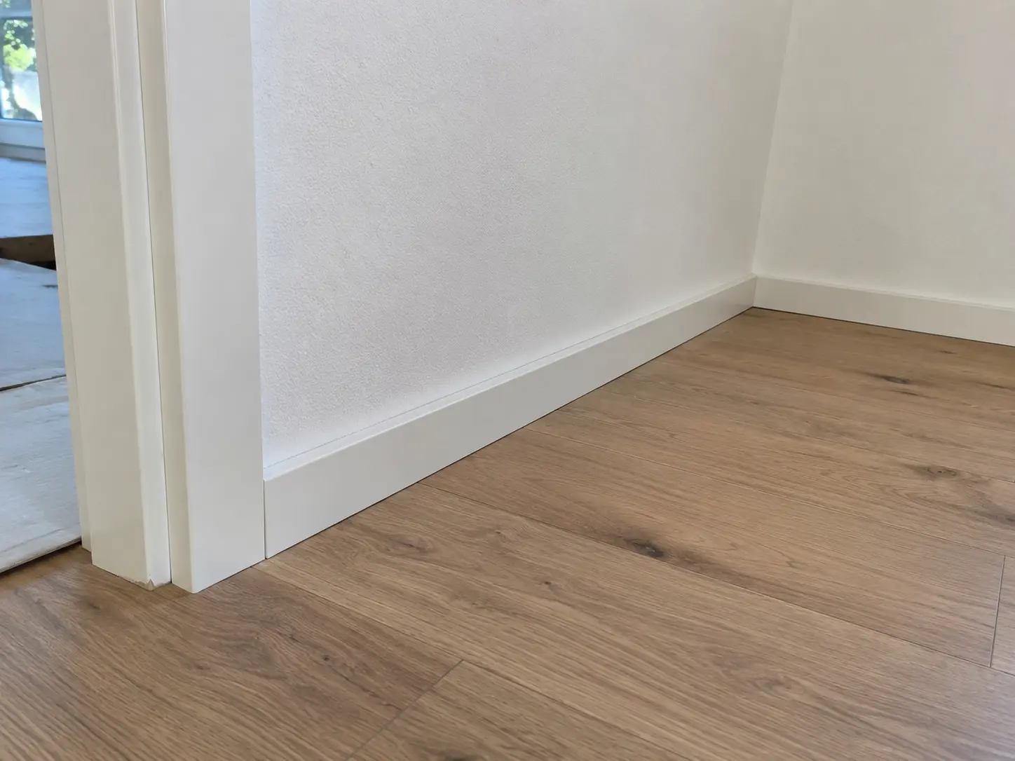 Weiße Sockelleiste am fertig verlegten Holzoptikboden neben einer Türzarge
