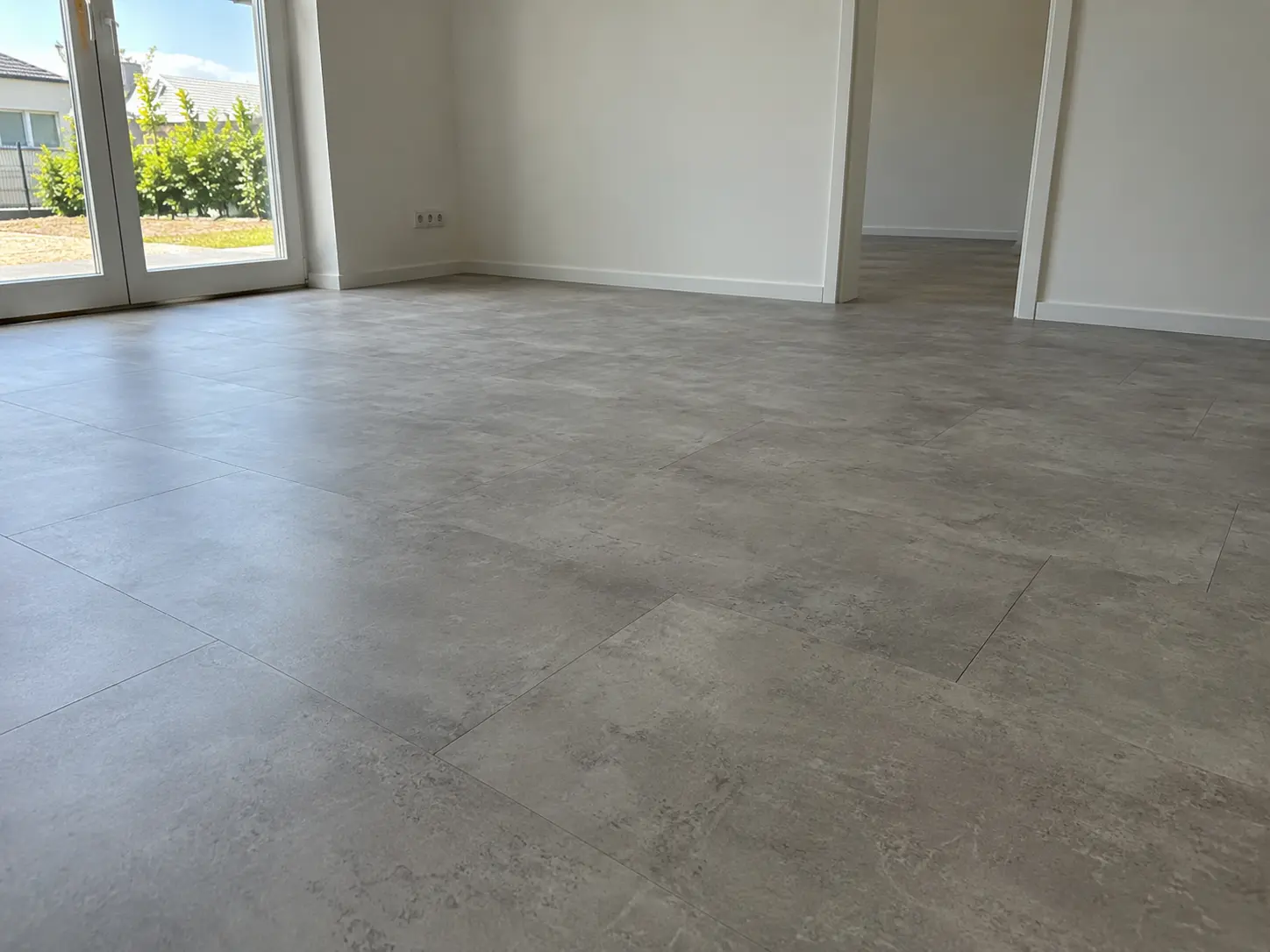 Leerer Raum mit neuem Vinylboden in Betonoptik und Terrassentür nach der Sanierung