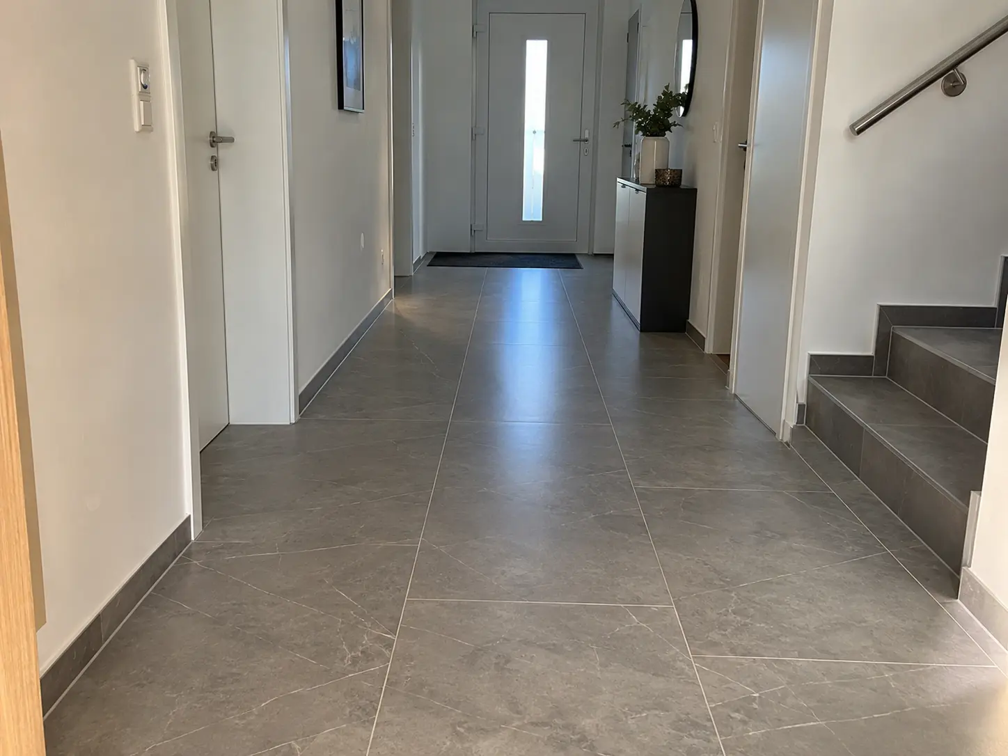 Flur mit großformatigen Fliesen in Steinoptik bis zur Haustür, rechts eine geflieste Treppe
