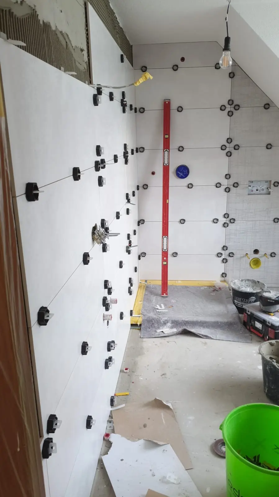 Dasselbe Dachbad im Rohbau mit frisch gesetzten Wandfliesen und Nivellierkeilen