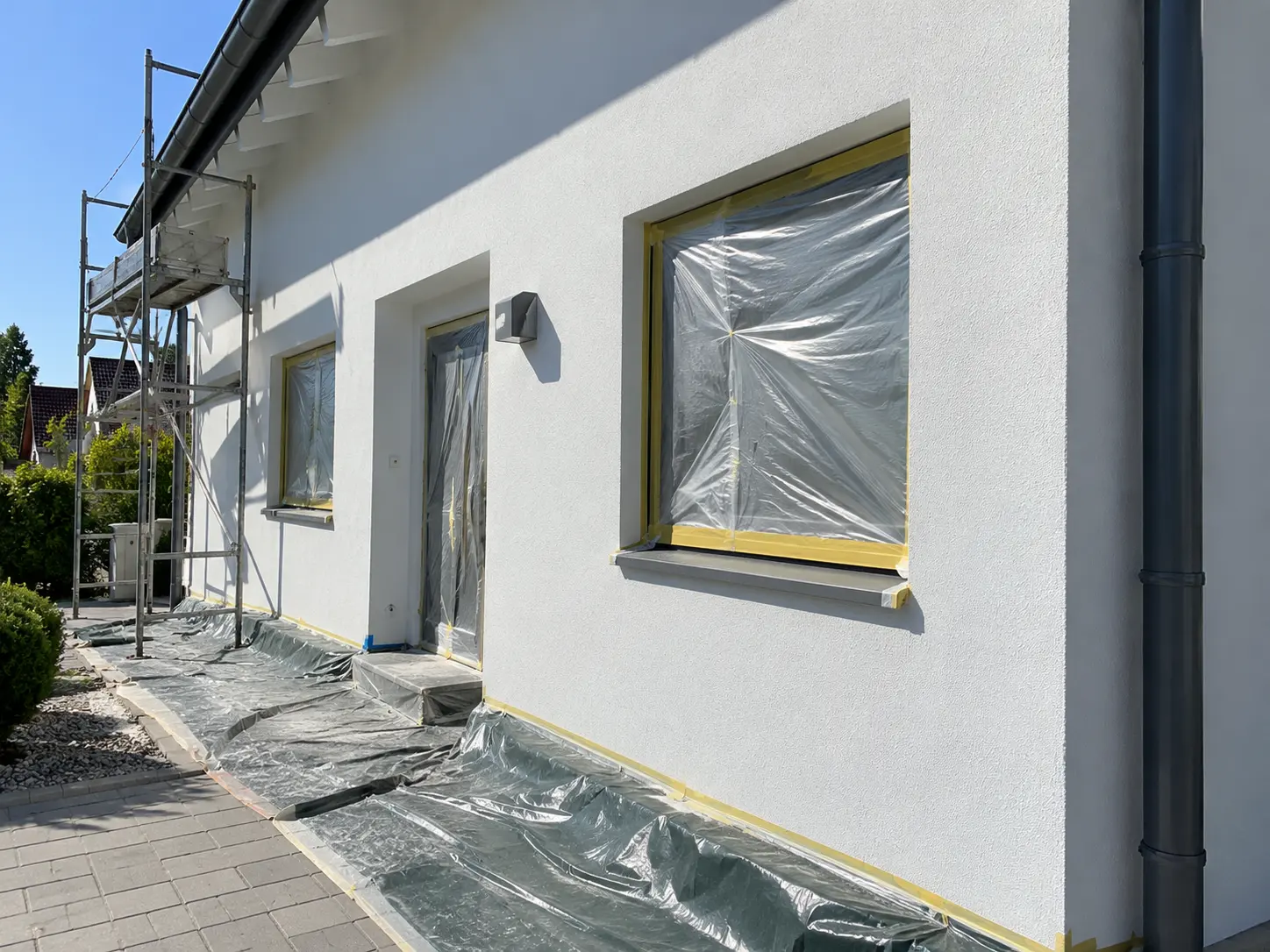 Frisch gestrichene weiße Fassade mit Gerüst und abgeklebten Fenstern