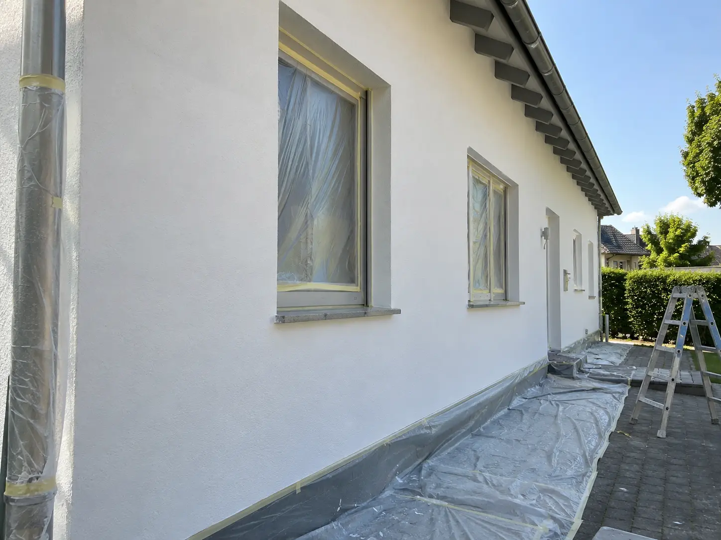 Frisch gestrichene weiße Fassade mit abgeklebten Fenstern und abgedecktem Sockel
