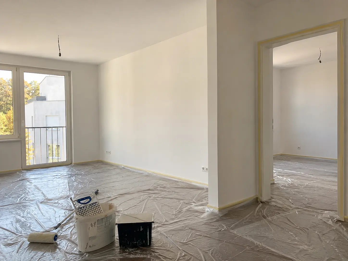 Frisch gestrichene Wohnung mit abgedecktem Boden, Farbrolle und Eimer