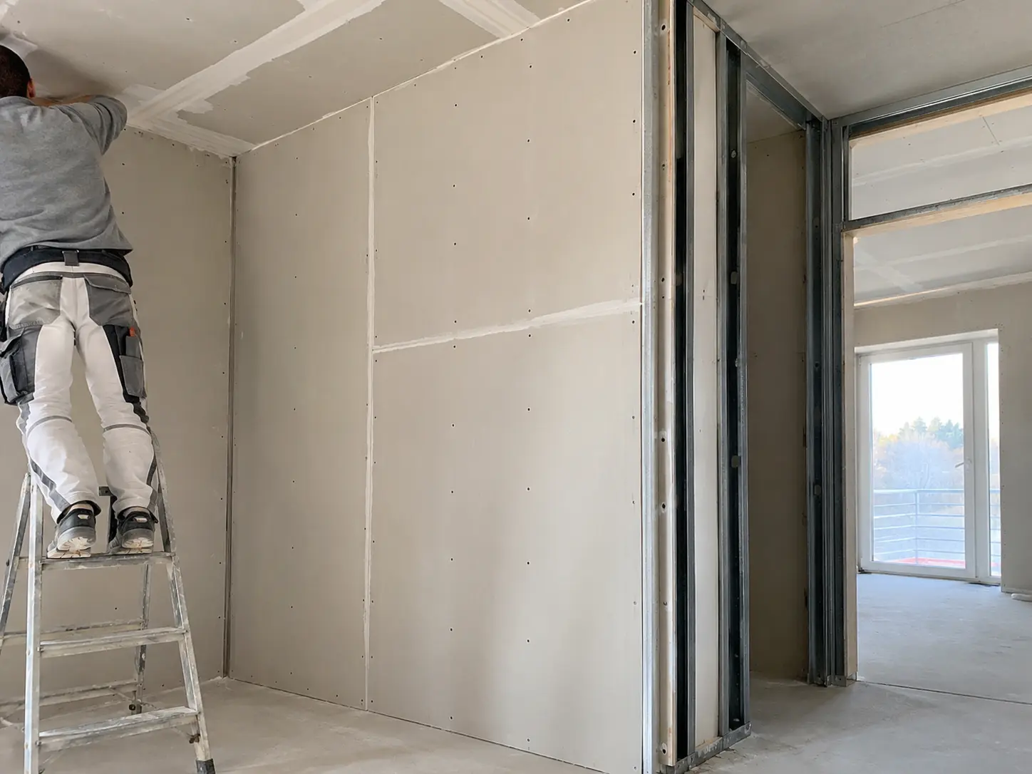 Trockenbauer auf der Leiter an einer neuen Ständerwand aus Gipskarton mit Metallprofilen